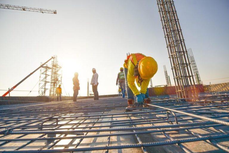Construction workers and engineers working on a commercial building site during sunset, installing rebar and inspecting progress