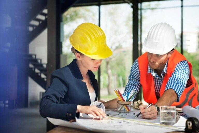 Two construction professionals reviewing blueprints at a job site with hard hats and safety gear
