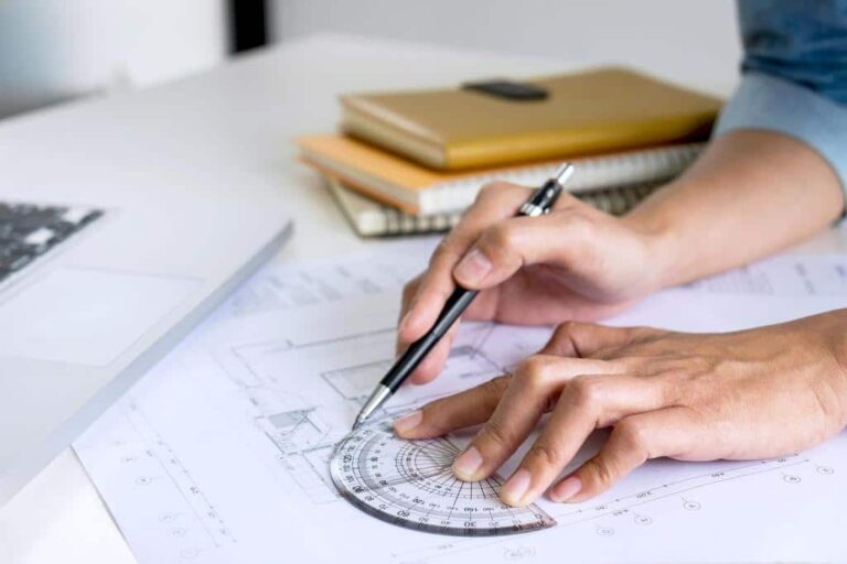 Close-up of architect’s hands using a protractor and pen to draw building plans on a blueprint in an office setting